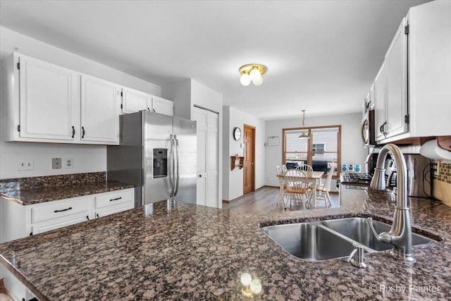 kitchen featuring stainless steel fridge with ice dispenser, dark stone counters, a sink, pendant lighting, and white cabinets