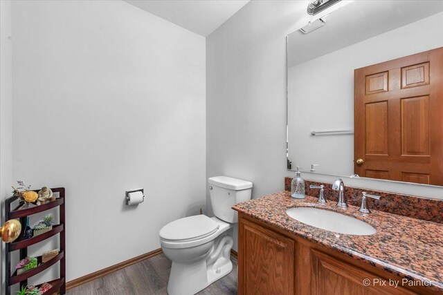 half bath with baseboards, toilet, vanity, and wood finished floors