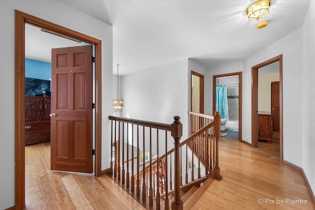 hall with baseboards, an upstairs landing, a chandelier, and light wood-type flooring
