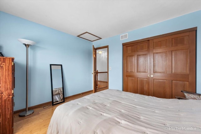 bedroom with attic access, baseboards, light wood finished floors, visible vents, and a closet
