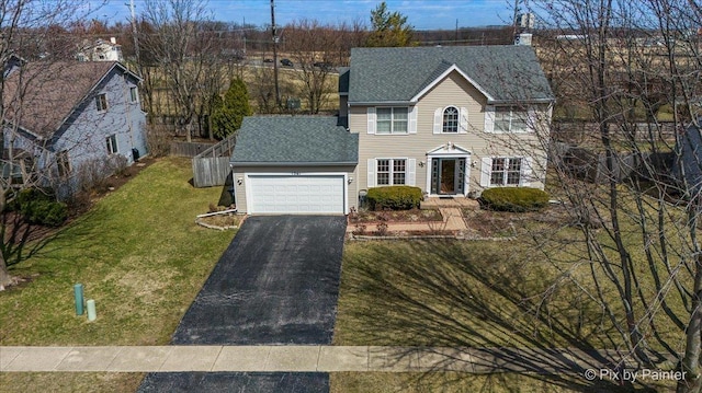colonial-style house with aphalt driveway, a garage, a shingled roof, and a front yard