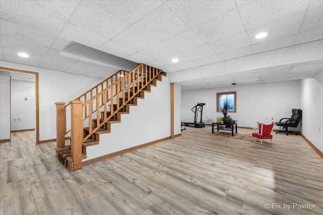 below grade area featuring stairs, wood finished floors, baseboards, recessed lighting, and a paneled ceiling