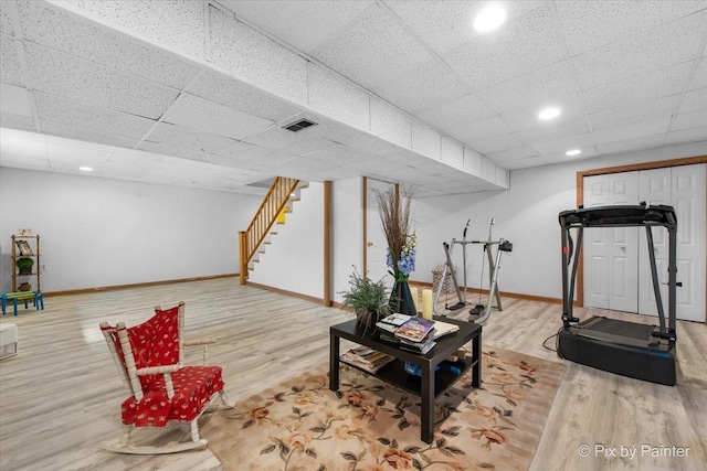 interior space featuring a drop ceiling, baseboards, light wood-style floors, and stairs