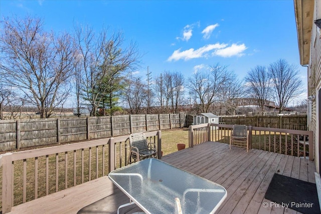 deck with a fenced backyard, outdoor dining area, an outbuilding, and a storage shed