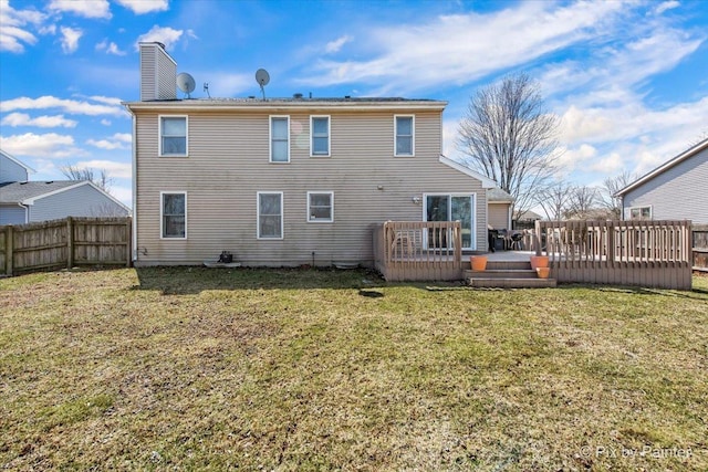 back of property featuring a wooden deck, a chimney, fence, and a lawn