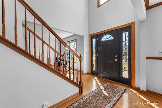 foyer featuring baseboards, a high ceiling, wood finished floors, and stairway