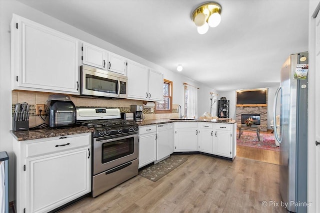 kitchen featuring white cabinetry, stainless steel appliances, light wood-style floors, a peninsula, and a glass covered fireplace