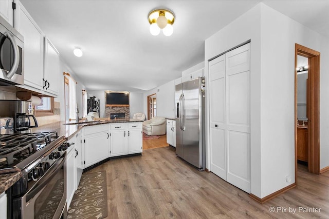 kitchen with open floor plan, light wood finished floors, white cabinets, a peninsula, and appliances with stainless steel finishes