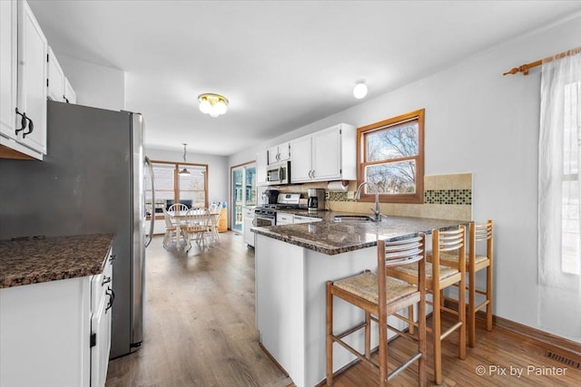 kitchen featuring a sink, wood finished floors, a peninsula, stainless steel appliances, and visible vents