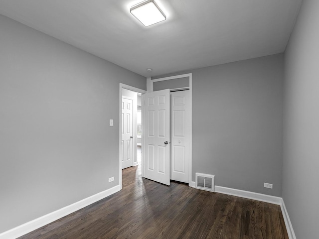 unfurnished bedroom with baseboards, dark wood-style floors, visible vents, and a closet