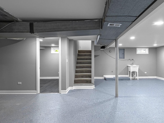 basement featuring stairs, baseboards, a sink, visible vents, and electric panel