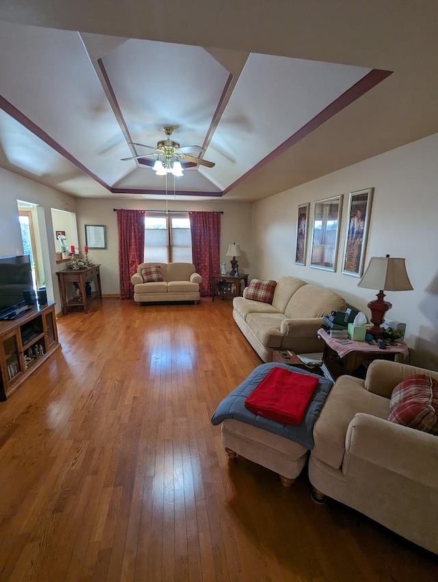 living room featuring a ceiling fan, light wood-type flooring, and a raised ceiling