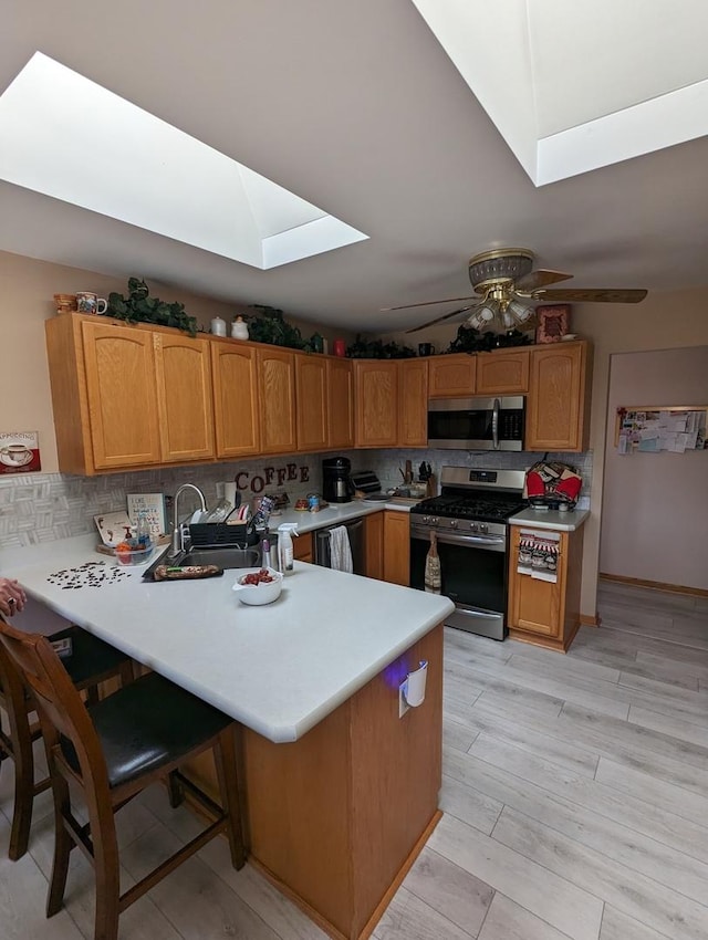 kitchen with light countertops, a ceiling fan, a skylight, a peninsula, and stainless steel appliances