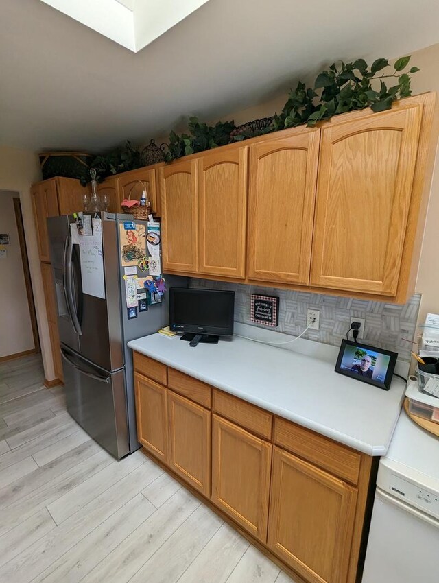 kitchen featuring light countertops, light wood-style flooring, backsplash, and freestanding refrigerator