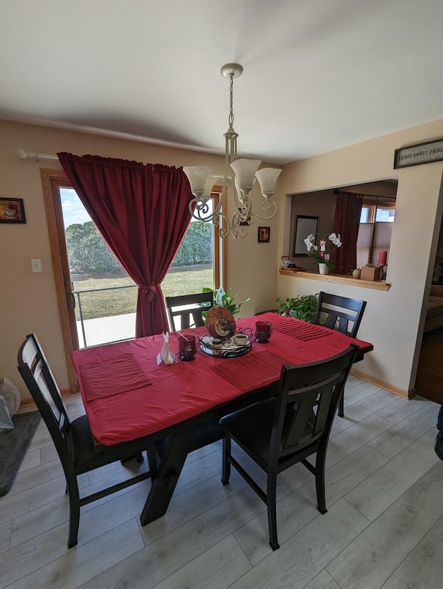 dining space with light wood-style flooring, a healthy amount of sunlight, and a notable chandelier