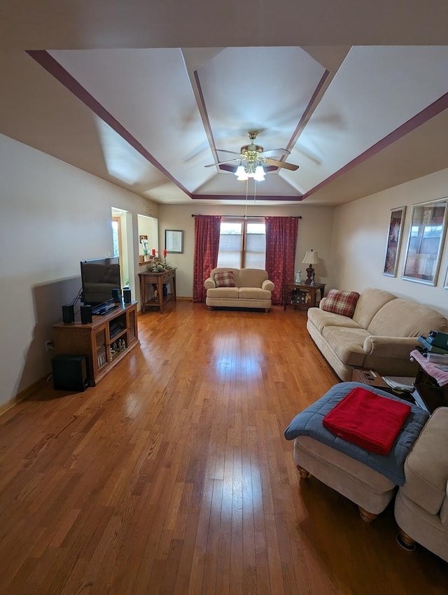 living area with a tray ceiling, ceiling fan, and wood-type flooring