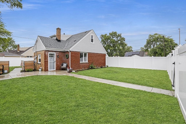 rear view of house featuring brick siding, a patio area, roof with shingles, and a chimney