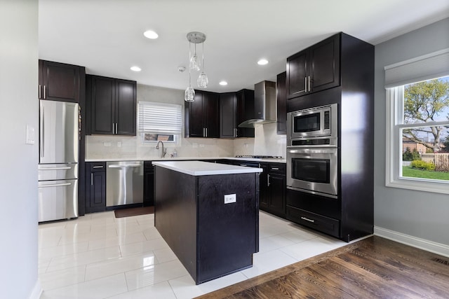 kitchen with tasteful backsplash, decorative light fixtures, wall chimney exhaust hood, light countertops, and stainless steel appliances