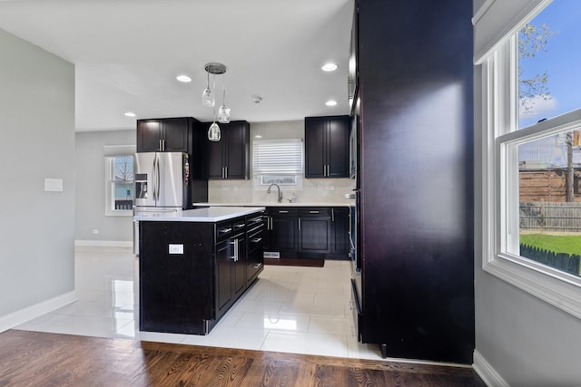 kitchen featuring stainless steel fridge with ice dispenser, a center island, light countertops, dark cabinetry, and baseboards