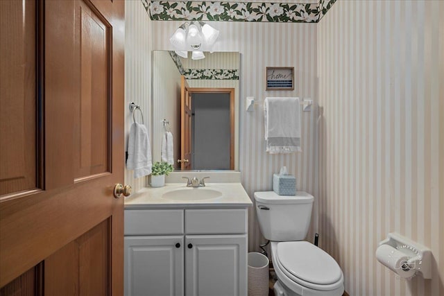 half bathroom with toilet, wallpapered walls, and vanity