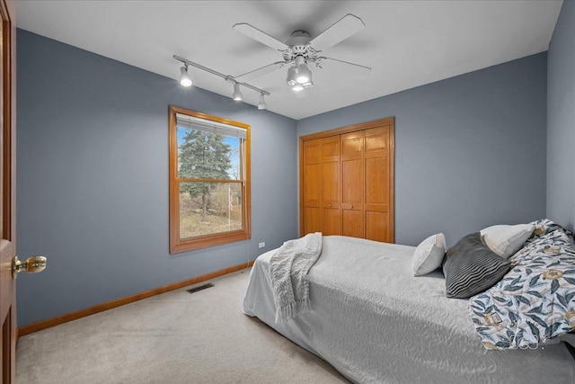 carpeted bedroom featuring a closet, baseboards, rail lighting, a ceiling fan, and visible vents