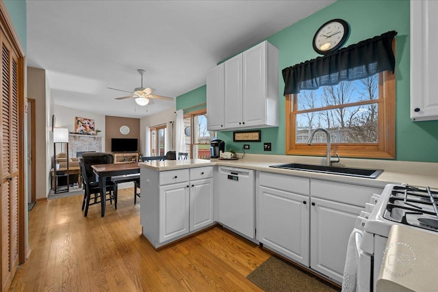 kitchen featuring white appliances, a peninsula, a ceiling fan, white cabinetry, and a sink