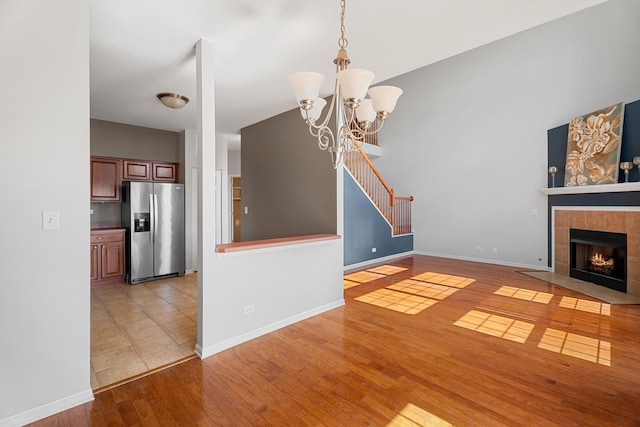 2366 Georgetown Cir, Aurora, IL 60503 - unfurnished living room featuring a tiled fireplace, baseboards, light wood-style floors, a towering ceiling, and an inviting chandelier