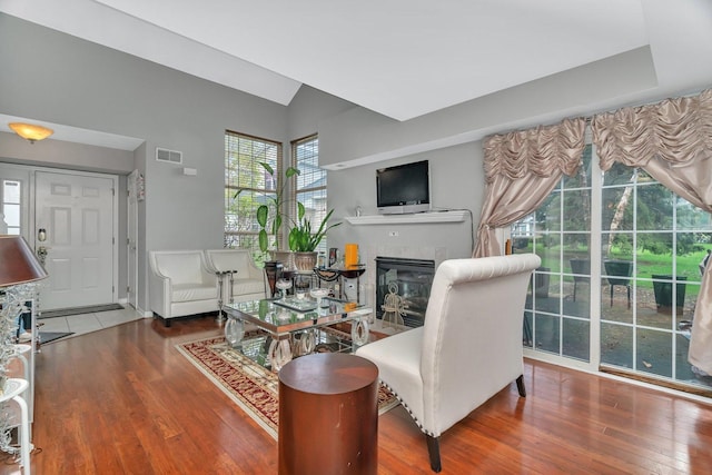 living room featuring a glass covered fireplace, wood finished floors, visible vents, and lofted ceiling