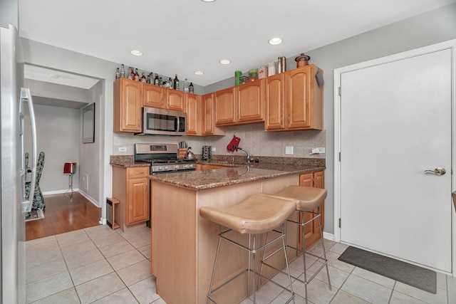 kitchen featuring tasteful backsplash, light tile patterned floors, stone countertops, a kitchen bar, and appliances with stainless steel finishes