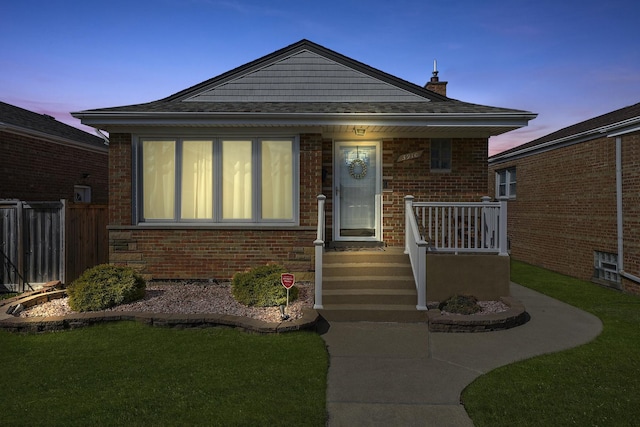 bungalow with brick siding, fence, covered porch, and a yard