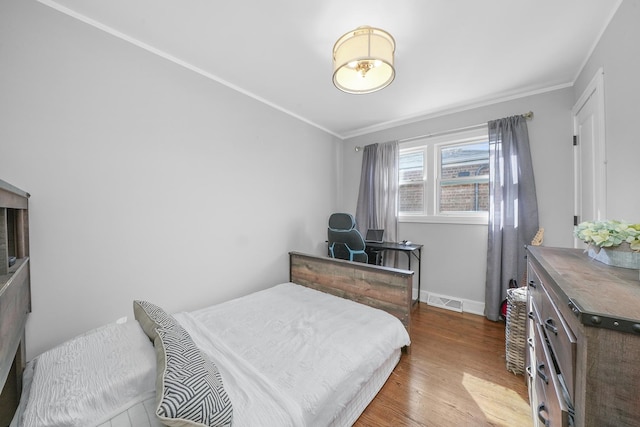 bedroom with wood finished floors, crown molding, baseboards, and visible vents