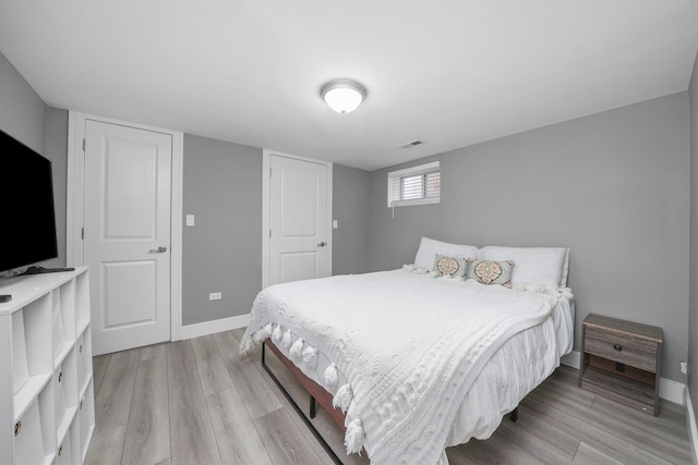 bedroom featuring baseboards, light wood finished floors, and visible vents