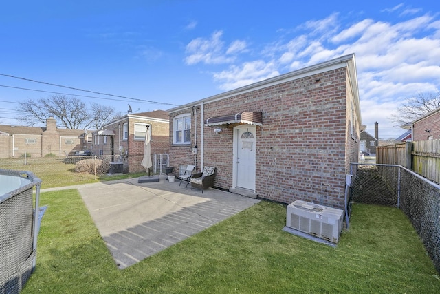 back of house with central air condition unit, a patio, a fenced backyard, brick siding, and a lawn