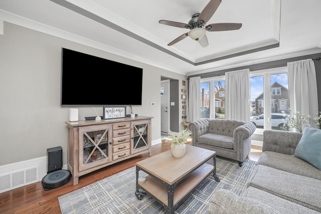 living area with baseboards, a raised ceiling, visible vents, a ceiling fan, and wood finished floors