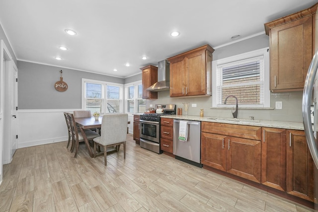 kitchen featuring decorative backsplash, brown cabinets, appliances with stainless steel finishes, a sink, and wall chimney range hood