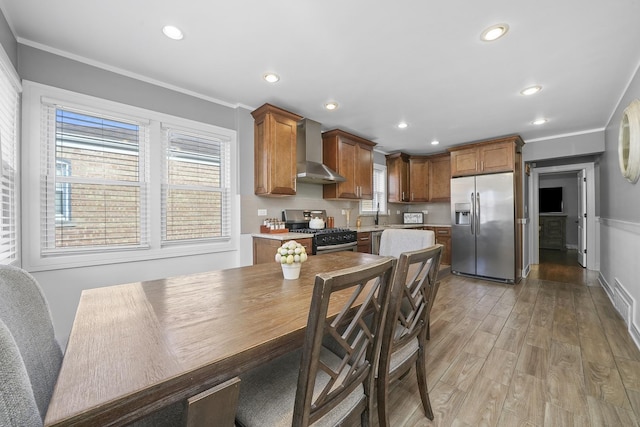 kitchen featuring light countertops, crown molding, appliances with stainless steel finishes, light wood-style floors, and wall chimney range hood