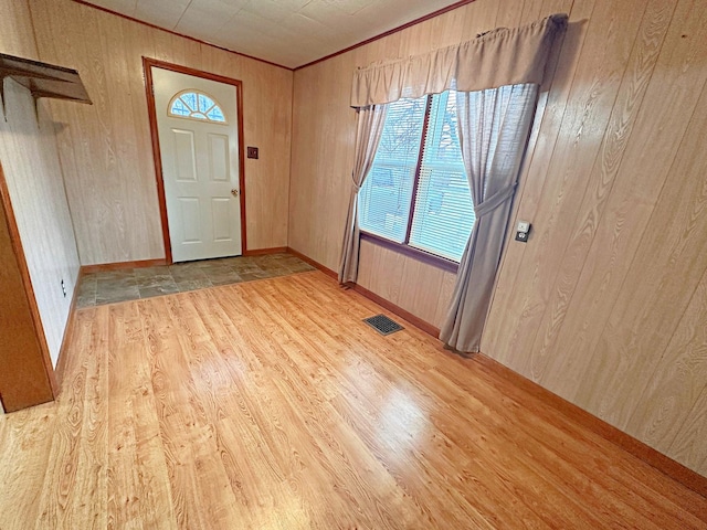 foyer entrance with crown molding, visible vents, wooden walls, and light wood-style flooring