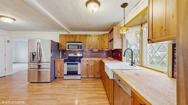 kitchen with light wood finished floors, a sink, tasteful backsplash, decorative light fixtures, and appliances with stainless steel finishes