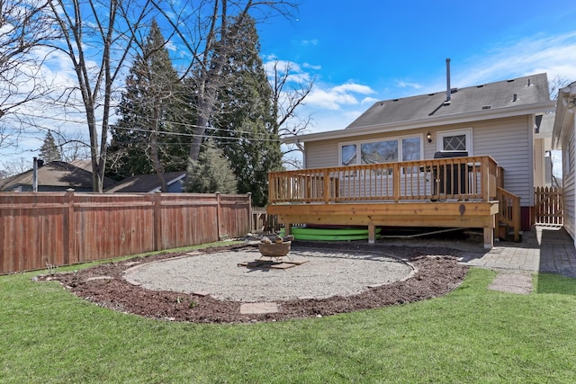 rear view of property featuring a fire pit, fence, a deck, and a lawn