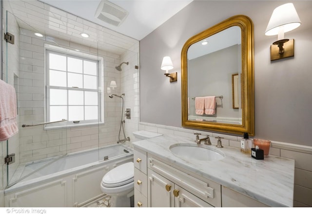 full bathroom featuring tile walls, toilet, visible vents, shower / bath combination with glass door, and vanity
