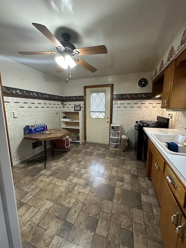 kitchen with light countertops, a sink, a ceiling fan, black range with gas cooktop, and tile walls