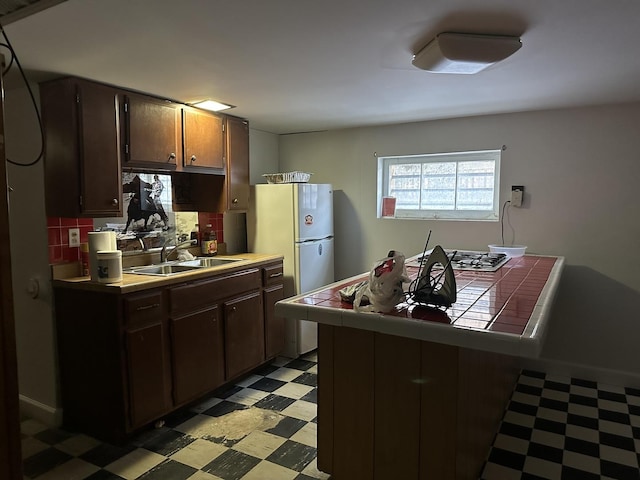 kitchen featuring a sink, tasteful backsplash, light floors, tile countertops, and dark brown cabinets