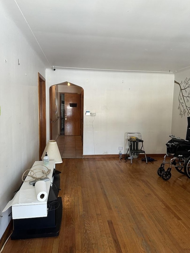 corridor featuring arched walkways, baseboards, and hardwood / wood-style flooring