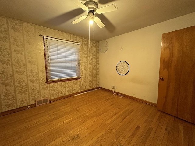 spare room featuring visible vents, baseboards, ceiling fan, wallpapered walls, and wood-type flooring
