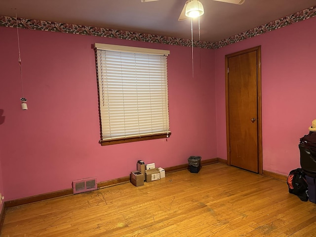 empty room featuring hardwood / wood-style floors, a ceiling fan, baseboards, and visible vents