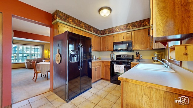 kitchen featuring brown cabinetry, light tile patterned floors, light countertops, black appliances, and a sink