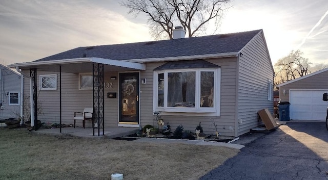 bungalow featuring an outbuilding, driveway, a front lawn, a garage, and a chimney