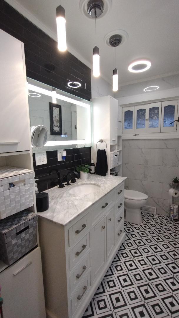 bathroom featuring tile walls, toilet, backsplash, vanity, and ornamental molding