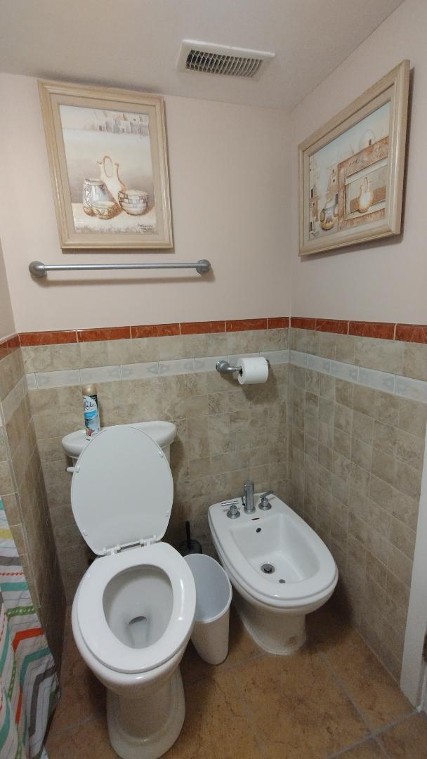 bathroom with tile walls, visible vents, toilet, a bidet, and wainscoting