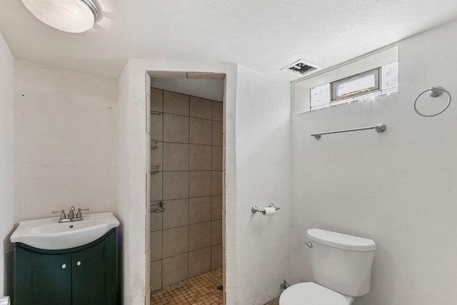 bathroom with toilet, tiled shower, and vanity